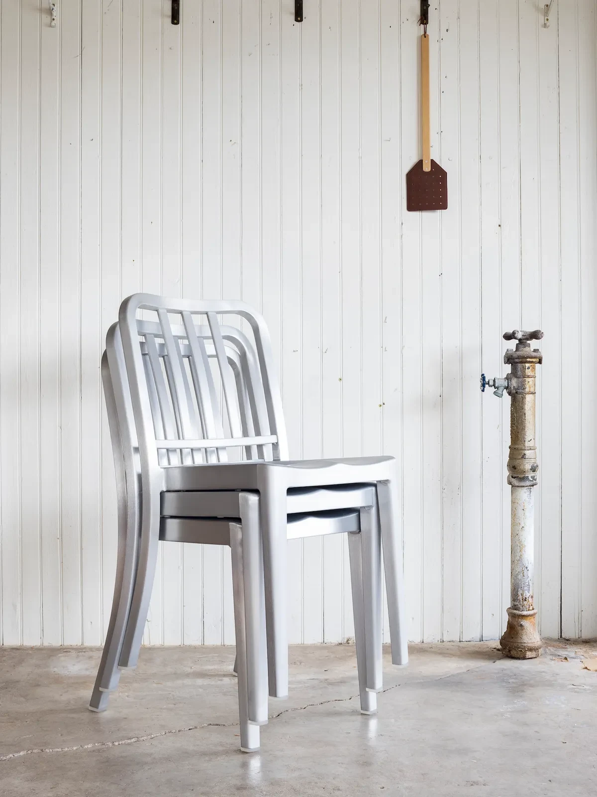 Stacked brushed aluminium Emeco chairs in front of a white wall