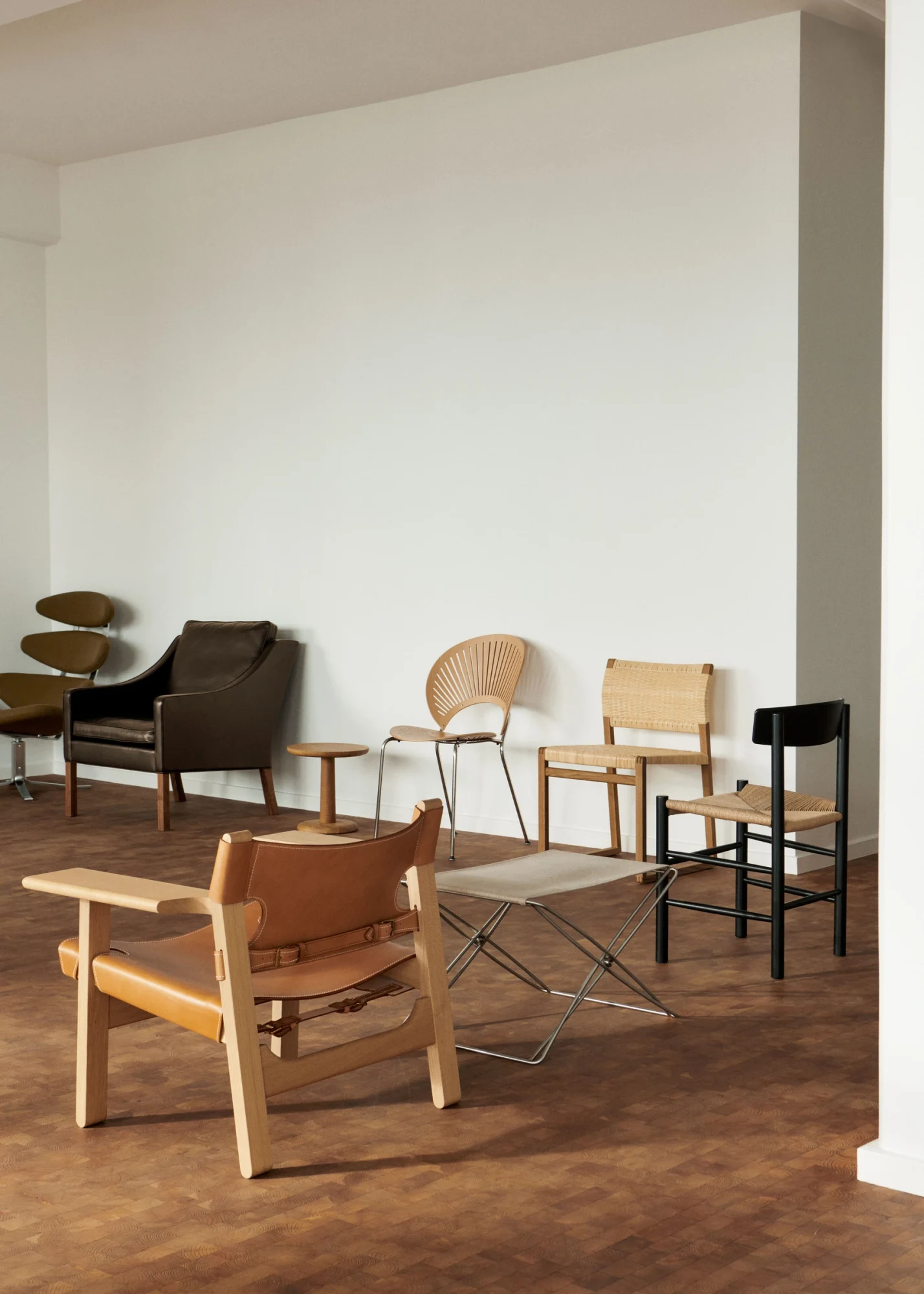 Spanish Chair in leather and wood in front of a row of other chairs against a white wall