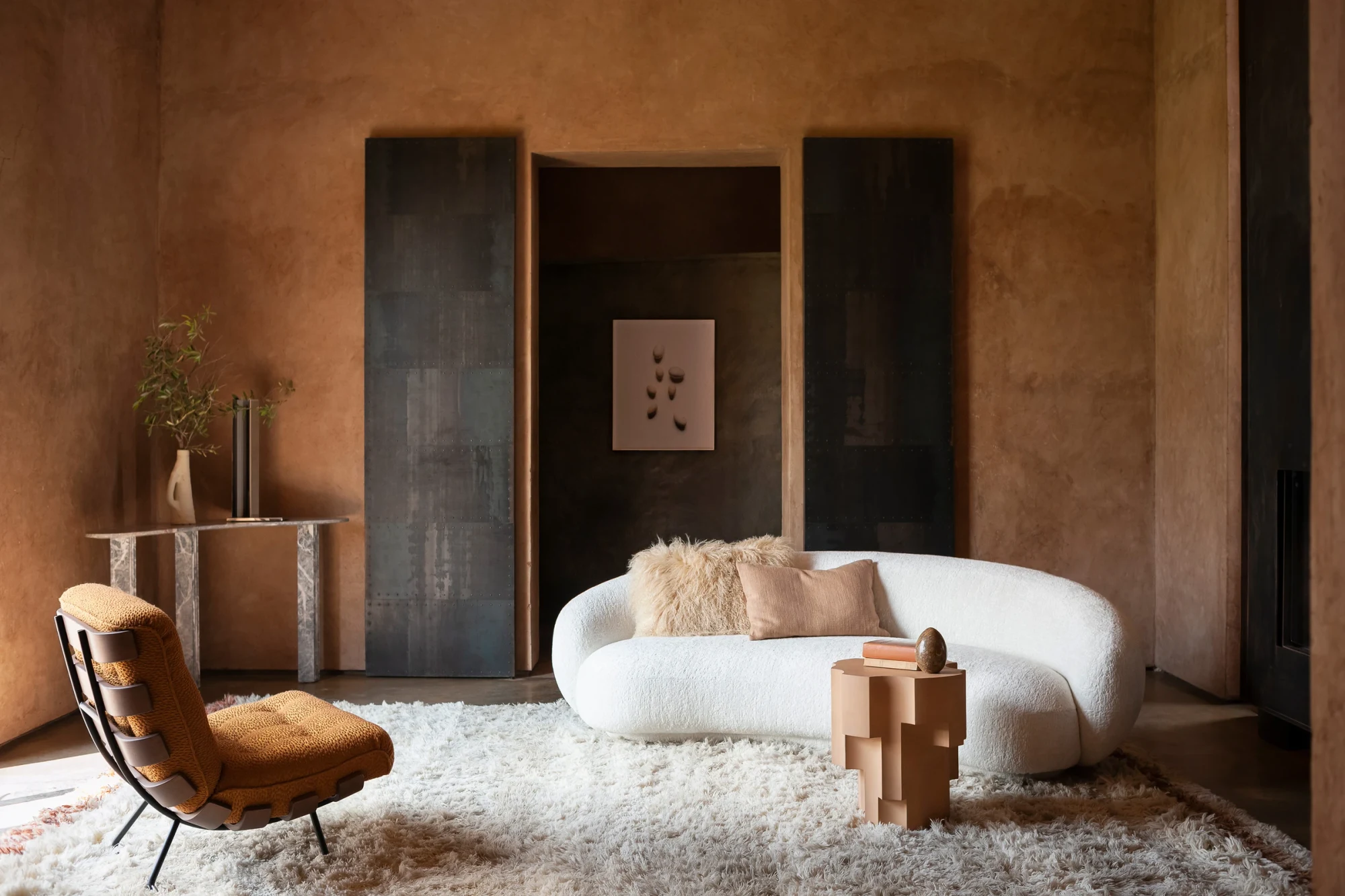 A white curved sofa, a chair and a wooden side piece in a room with a large rug