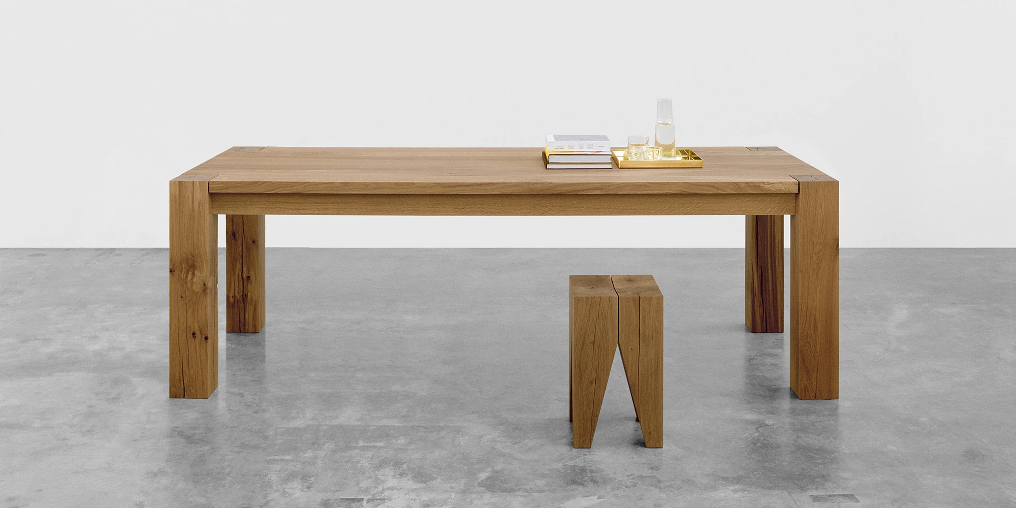 A wooden table with a stool on a concrete floor in front of a white wall