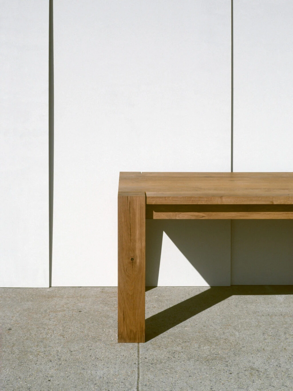 A close view of a corner of a wooden table in front of a white wall