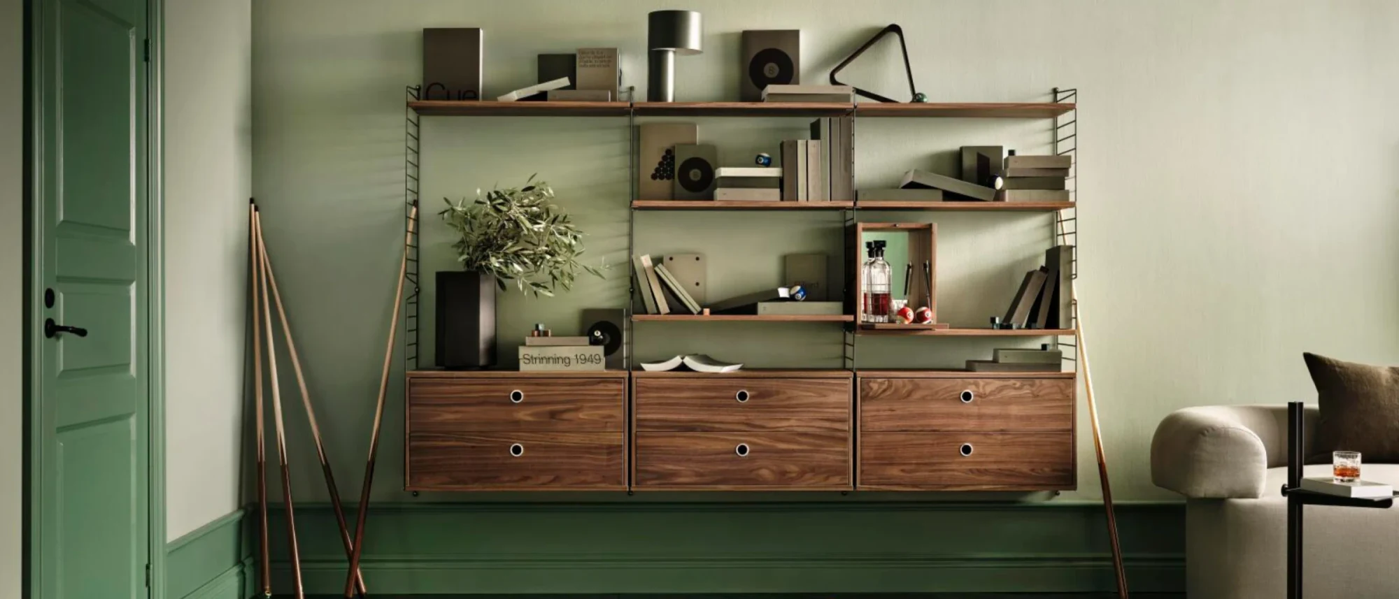 String shelving system with walnut cabinets in a green room