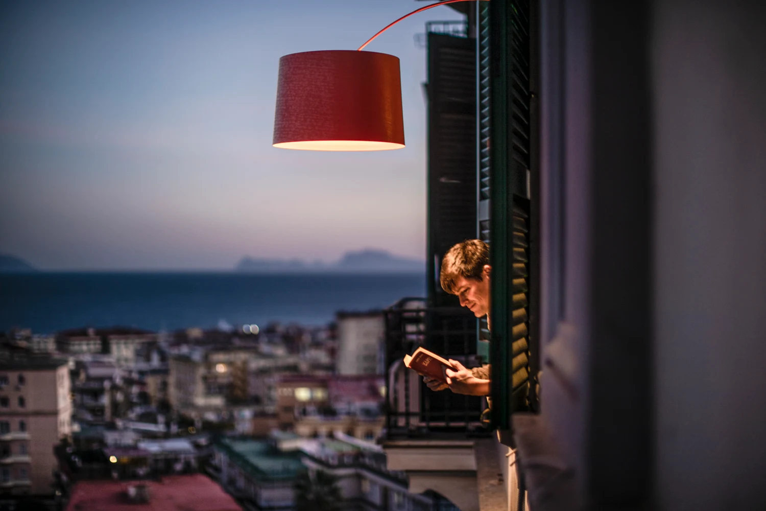Red arc floor lamp over a balcony at dusk