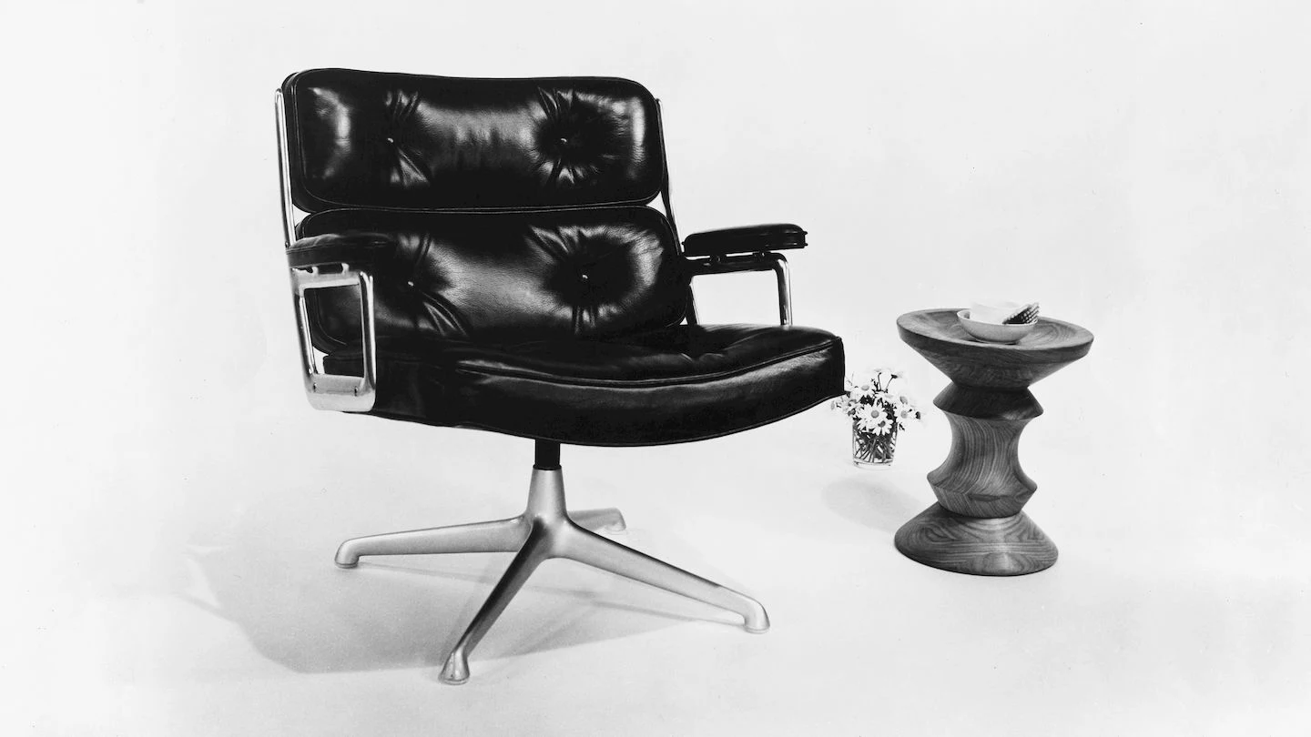 Black-and-white photograph of a cushioned chair on a four-star swivel base beside a small turned stool
