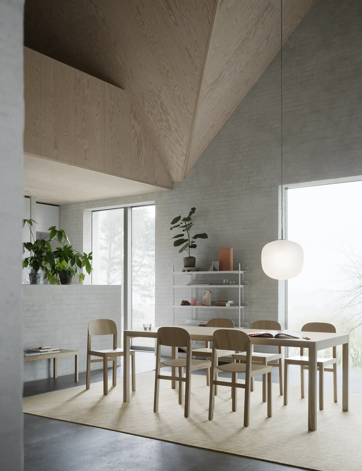 A long table with chairs under a large round pendant lamp in a room with a pitched ceiling