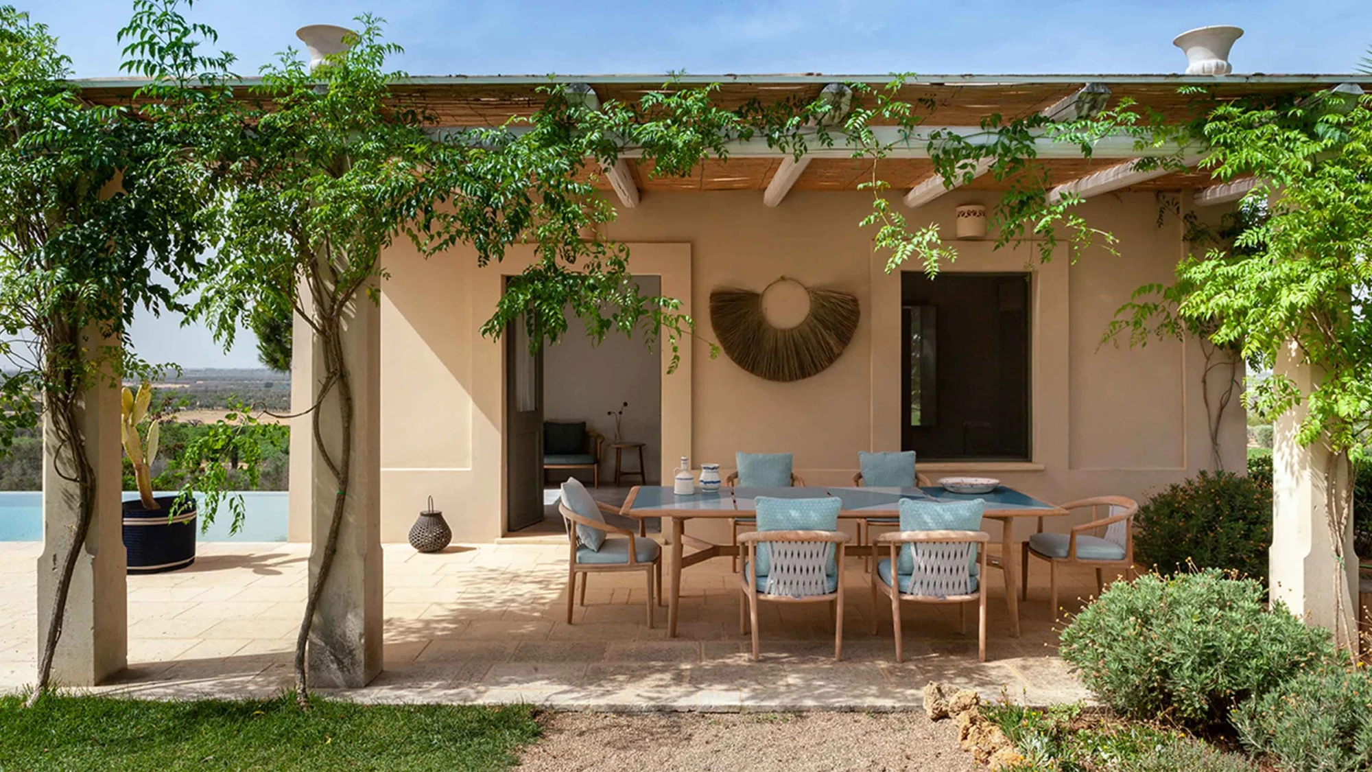 Outdoor armchairs around a table under a pergola with climbing plants