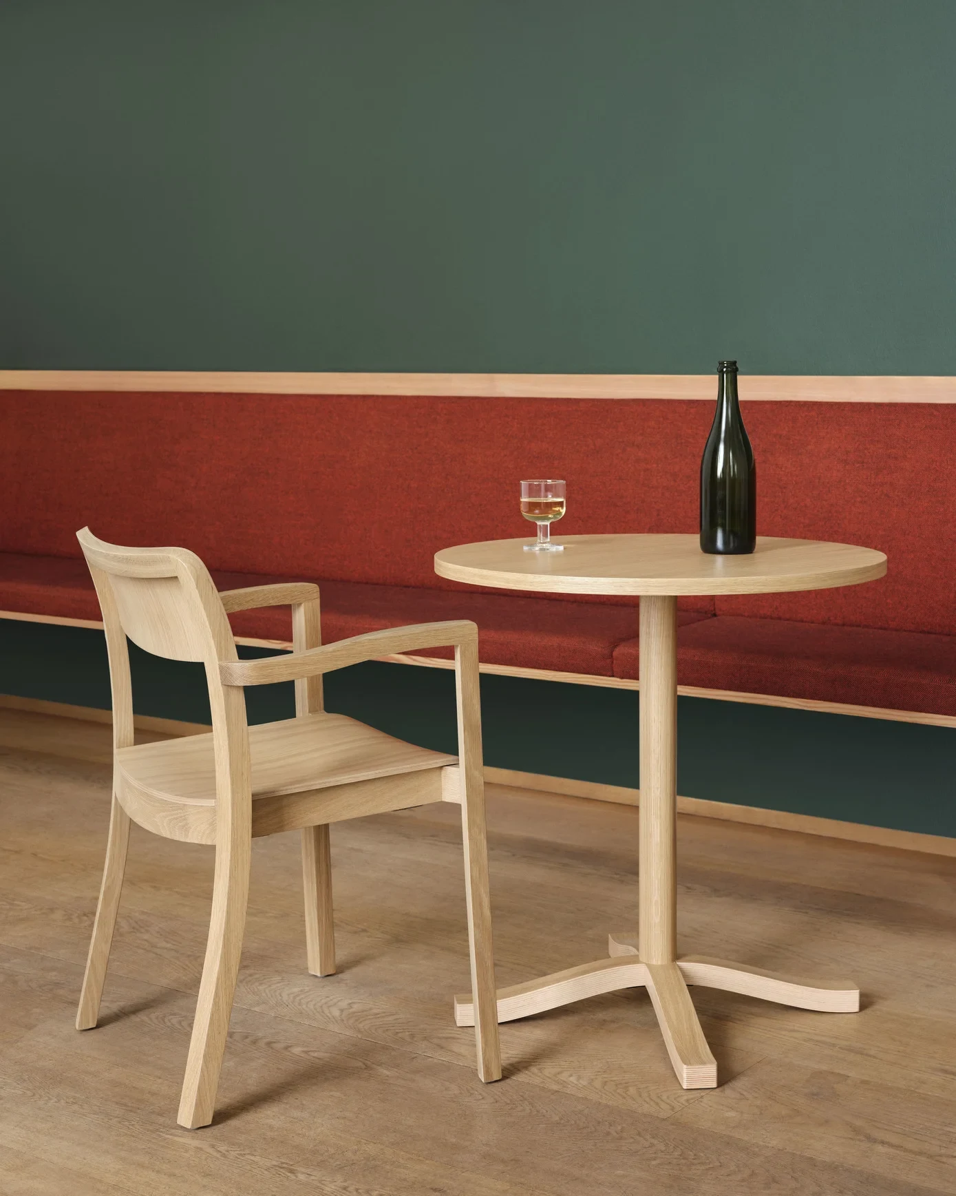 A chair with armrests beside a round table with a glass and a bottle