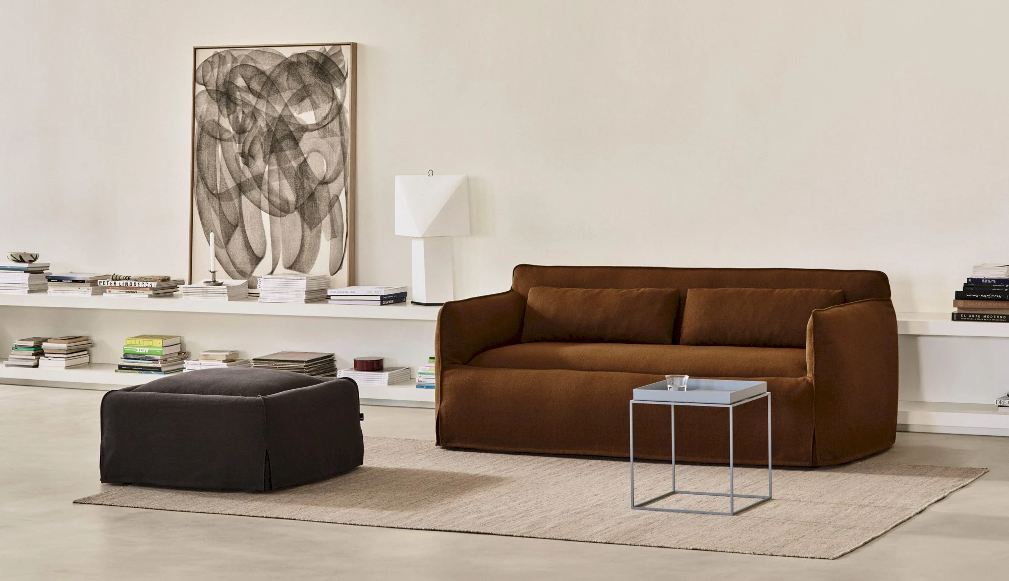 A Mimi sofa and an ottoman in a room with a wall picture and shelves