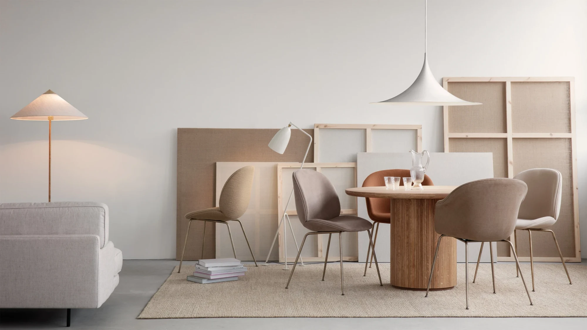 Round table with chairs around it and a floor lamp beside it, in front of canvases leaning against a wall