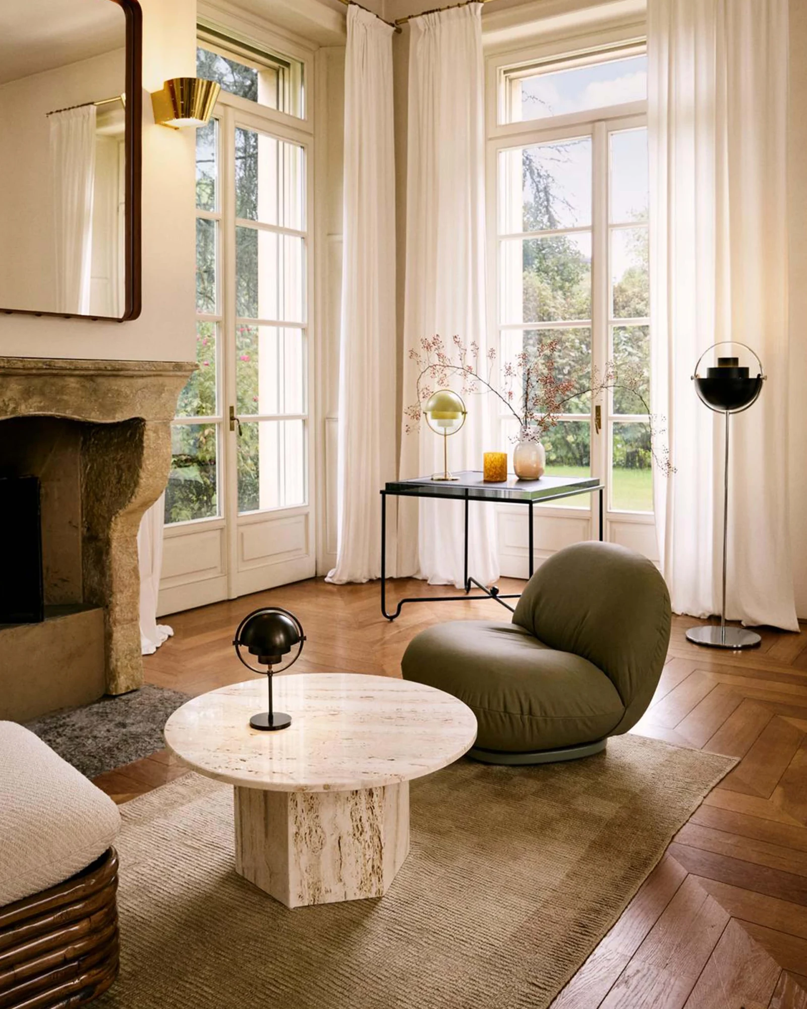 Round table with a pale stone top and a hexagonal base, beside an armchair and a lamp, in a room