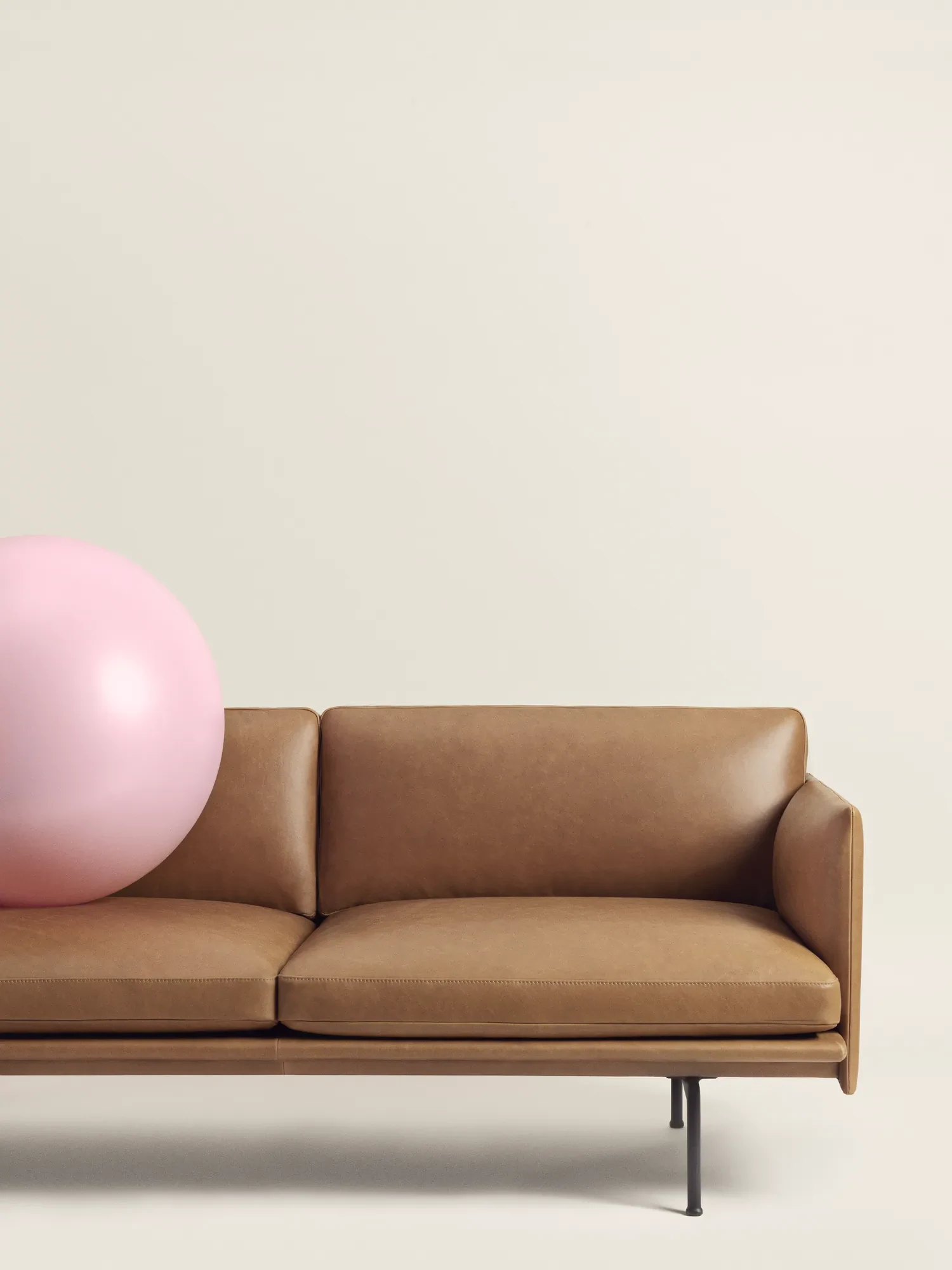 Outline Sofa with a large ball resting on its seat in a plain studio setting