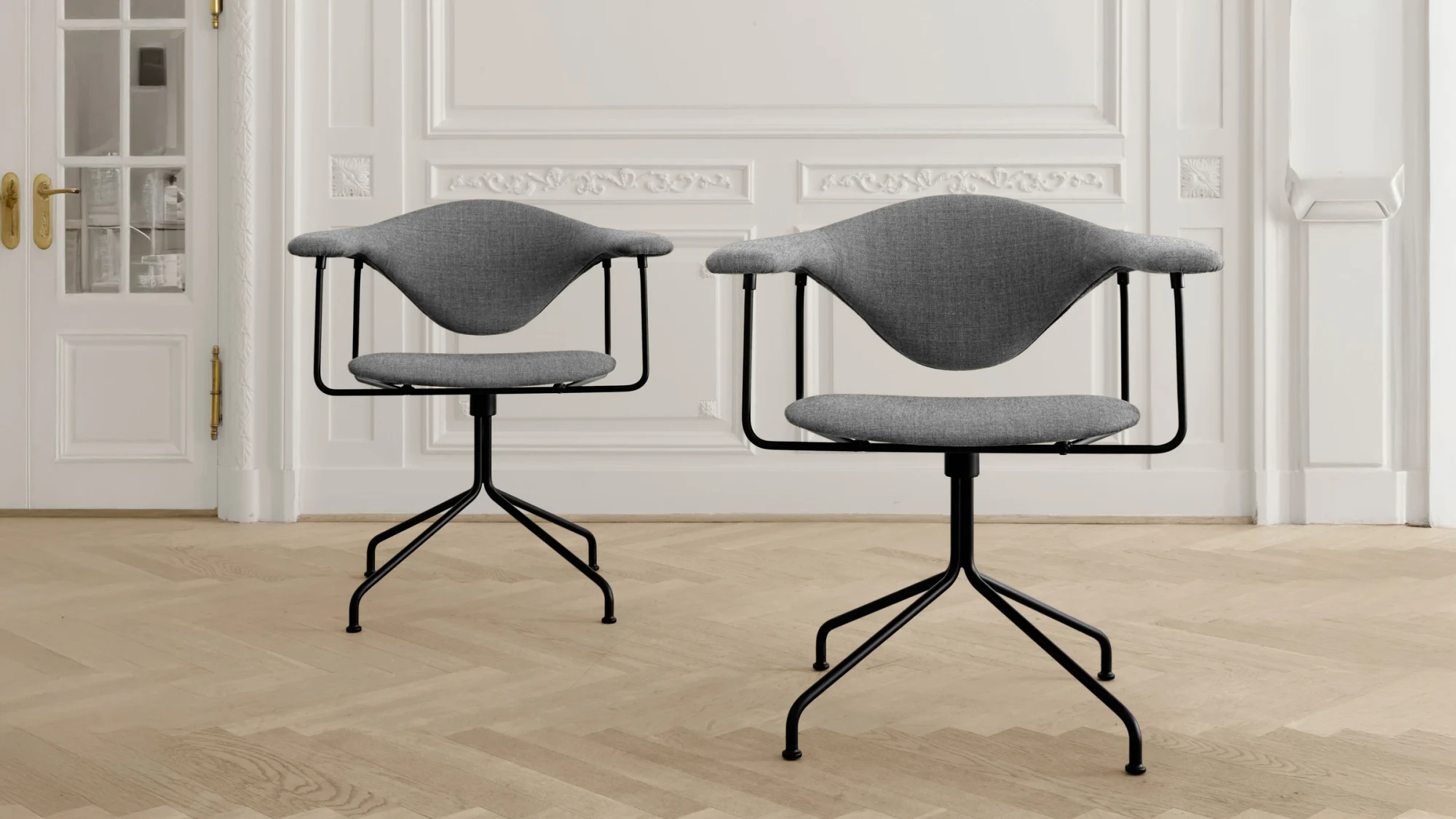 Two upholstered swivel chairs with black bases in a room with white panelled walls