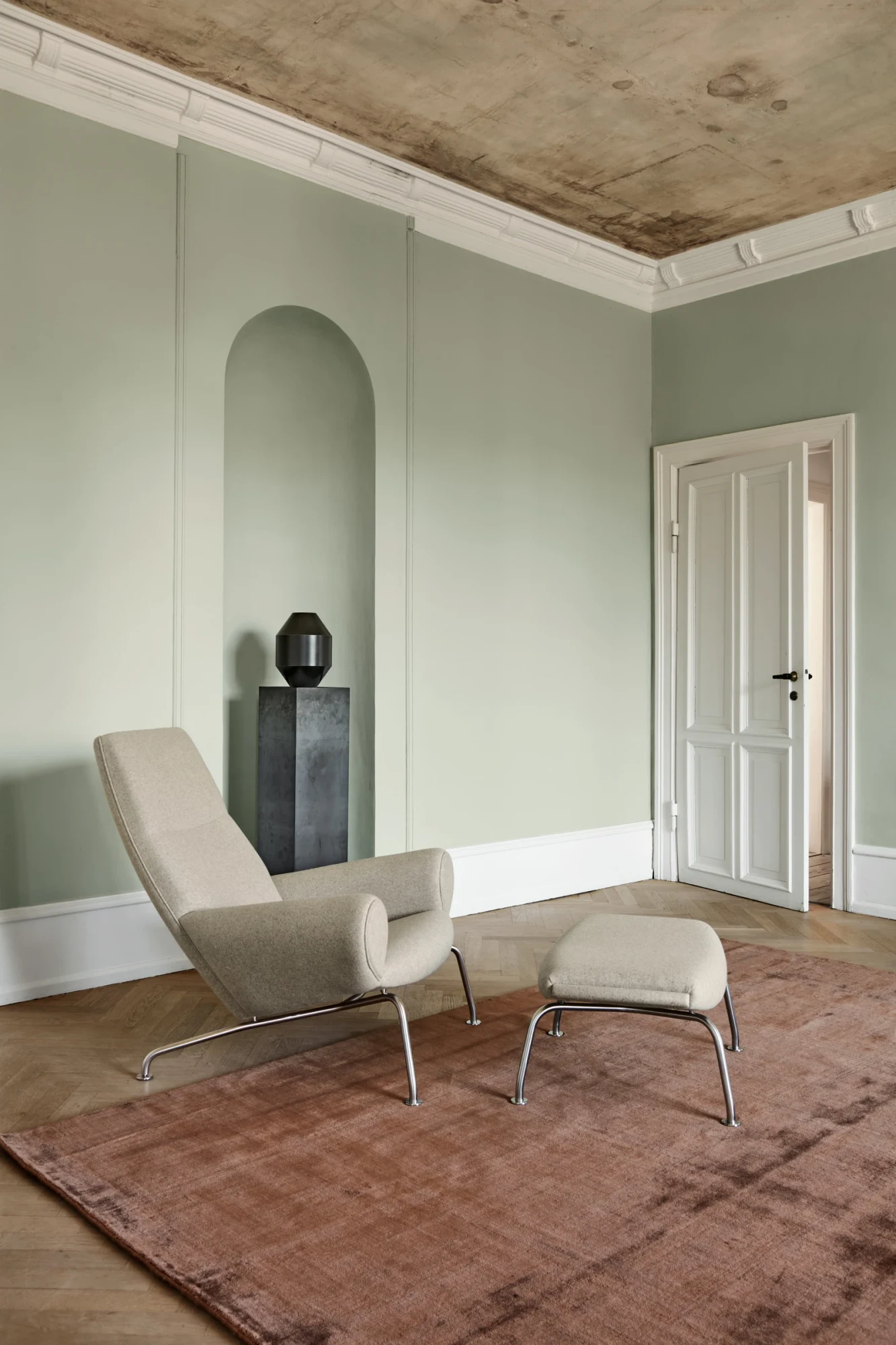 The Queen Chair in a pale fabric beside a footstool in a room with tall windows