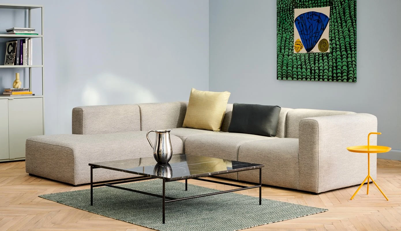 Corner sofa in a pale covering with a low table, a yellow side table and a green picture on the wall