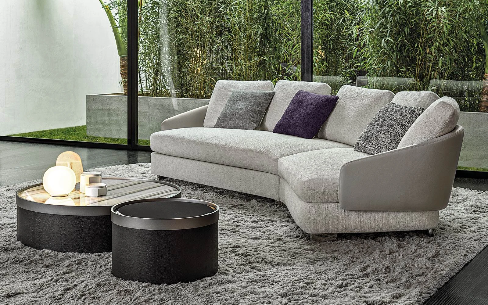 Lawson sofa with a curved end, cushions and two round tables on a rug, official Minotti photo