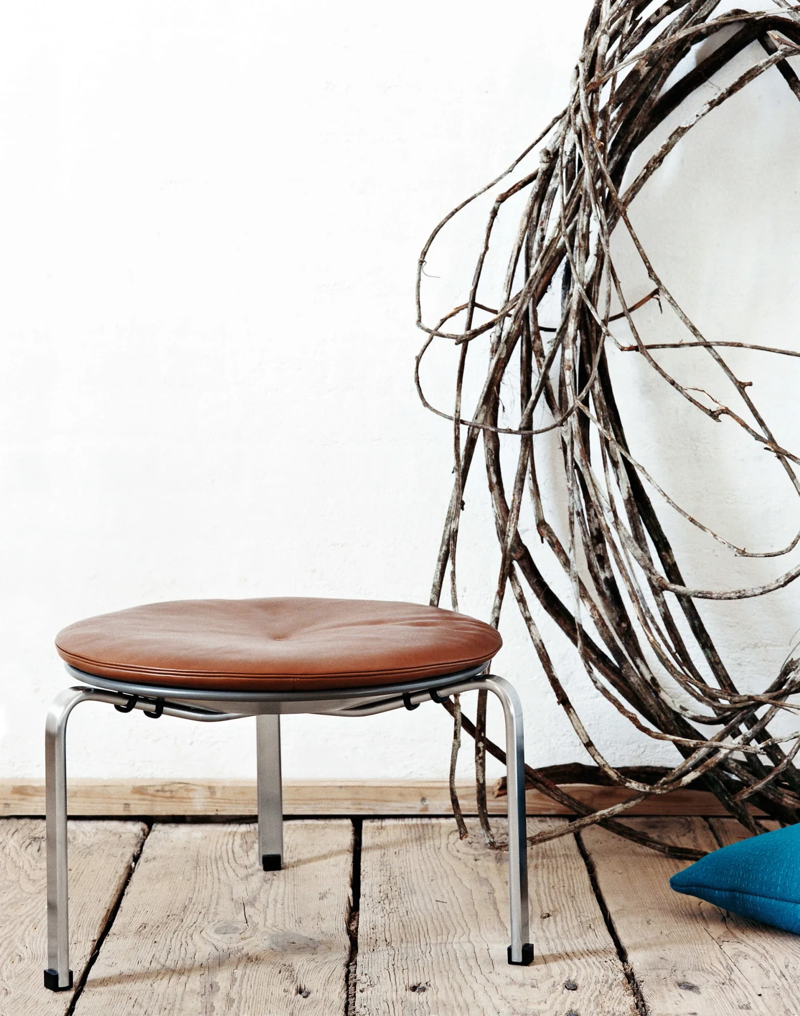 A round cushioned stool on three legs beside a tangle of branches