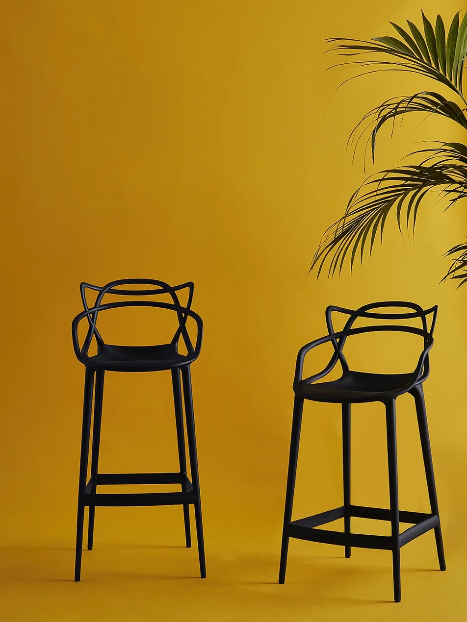 Two stools standing in front of a plain wall beside a palm leaf
