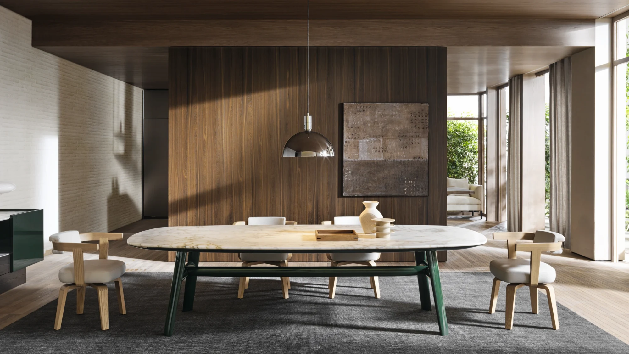 Long oval table with chairs around it and a hanging lamp, in front of a panelled wall