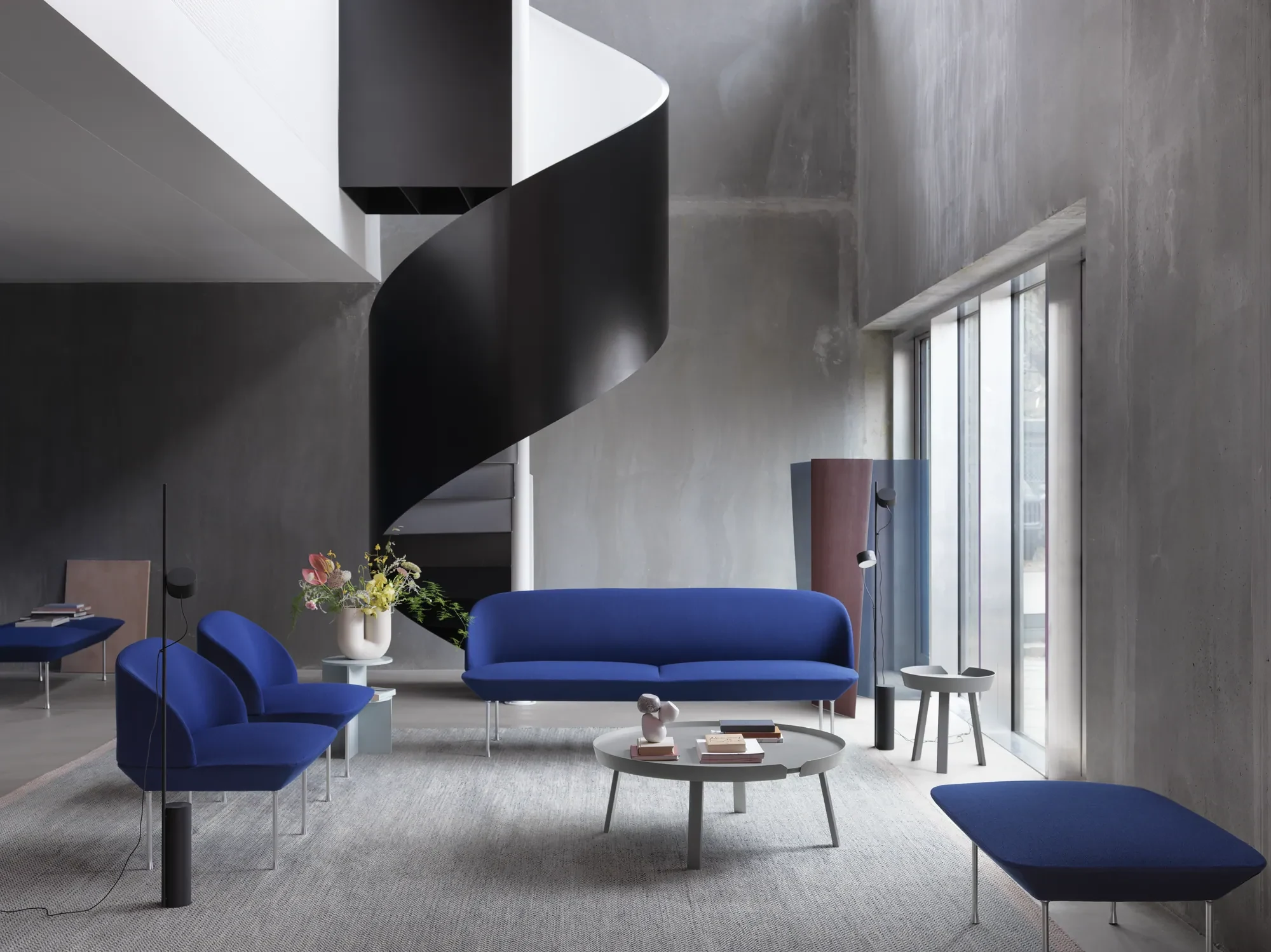 Sofa, lounge chairs and a pouf around a round low table beside a black spiral staircase