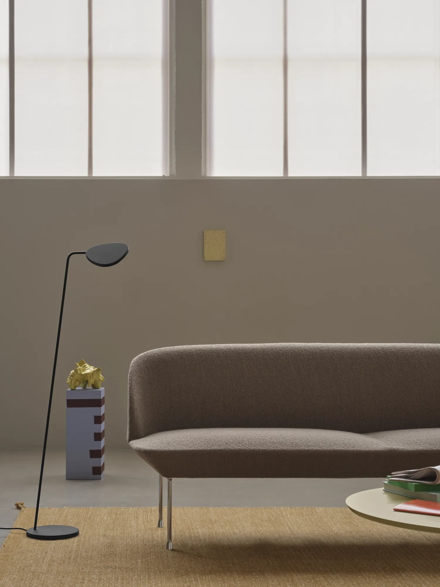 Three-seat sofa beside a floor lamp and a low round table in a room with tall windows