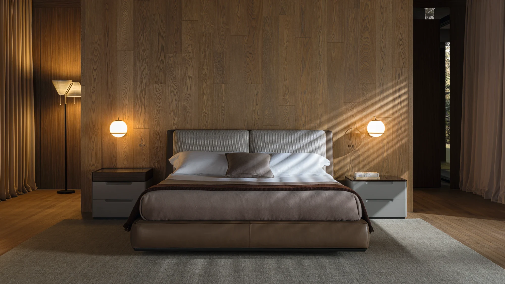 A bed with a rectangular headboard and two cushions between two bedside tables, with a wall lamp on each side