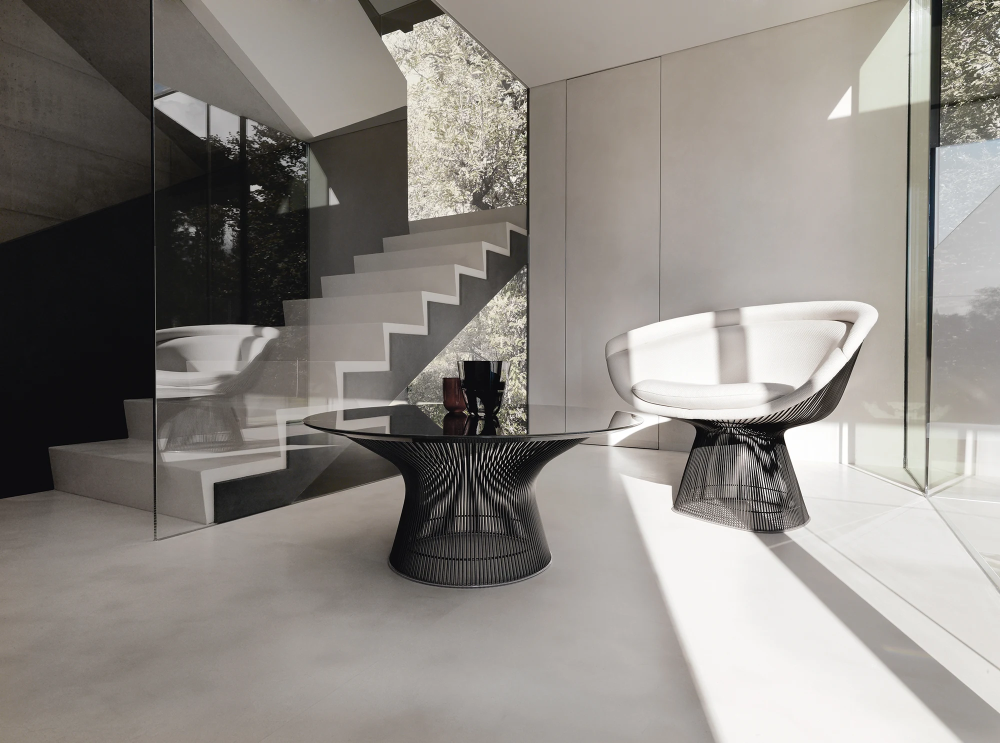 Coffee table beside a Platner lounge chair in a room with a staircase (official Knoll photograph, caption 10405 Platner Lounge Chair and Coffee Table)
