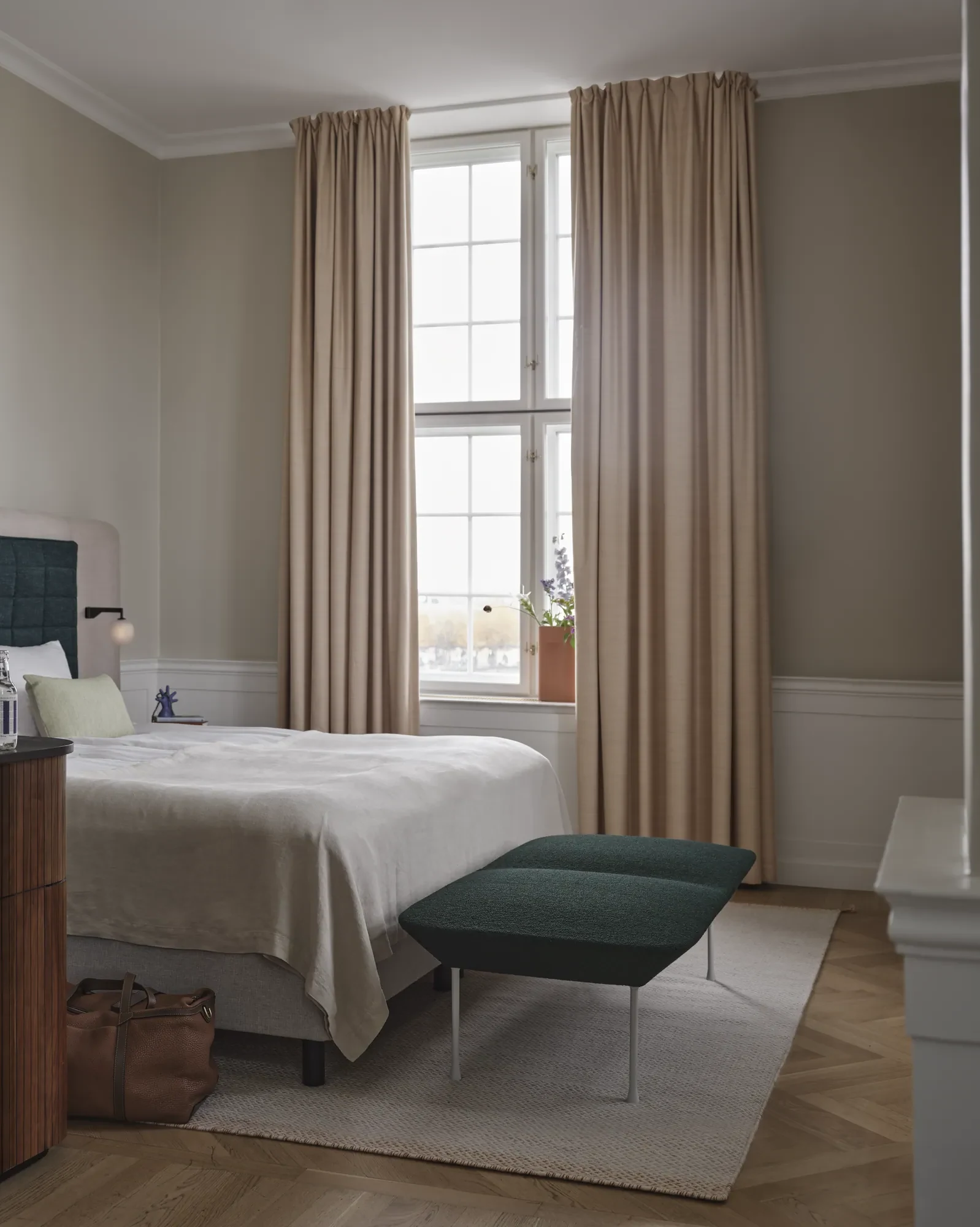 Oslo Bench at the foot of a bed in a room with tall windows and curtains