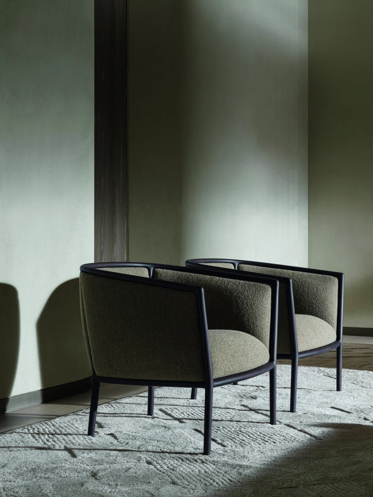 Two Margou armchairs with dark frames on a patterned rug in front of a plain wall