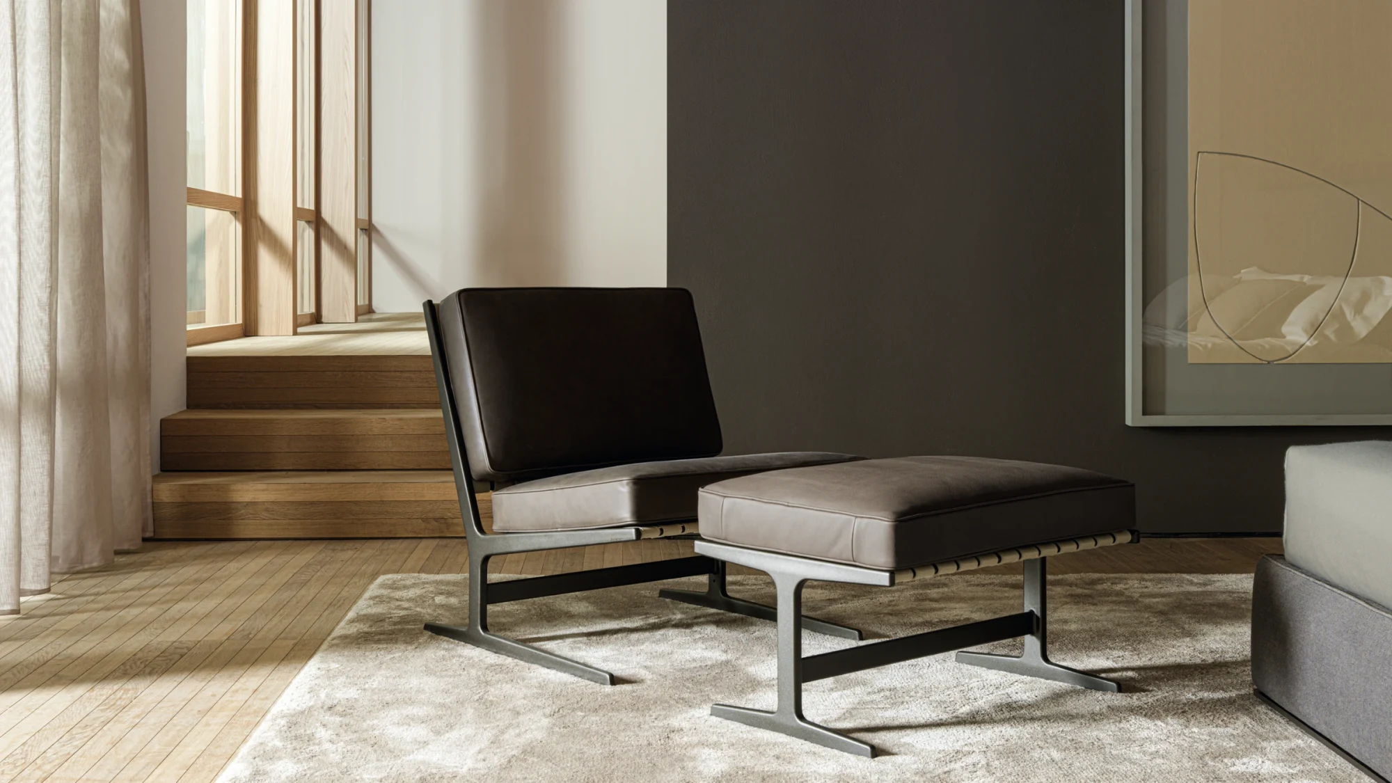 A Paula armchair and matching pouf on a light rug, with steps and a window behind