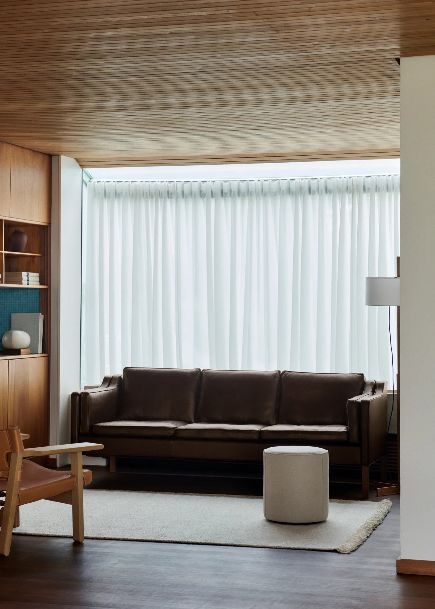 Le canapé dans une pièce au plafond en bois, avec un pouf devant et une chaise à gauche
