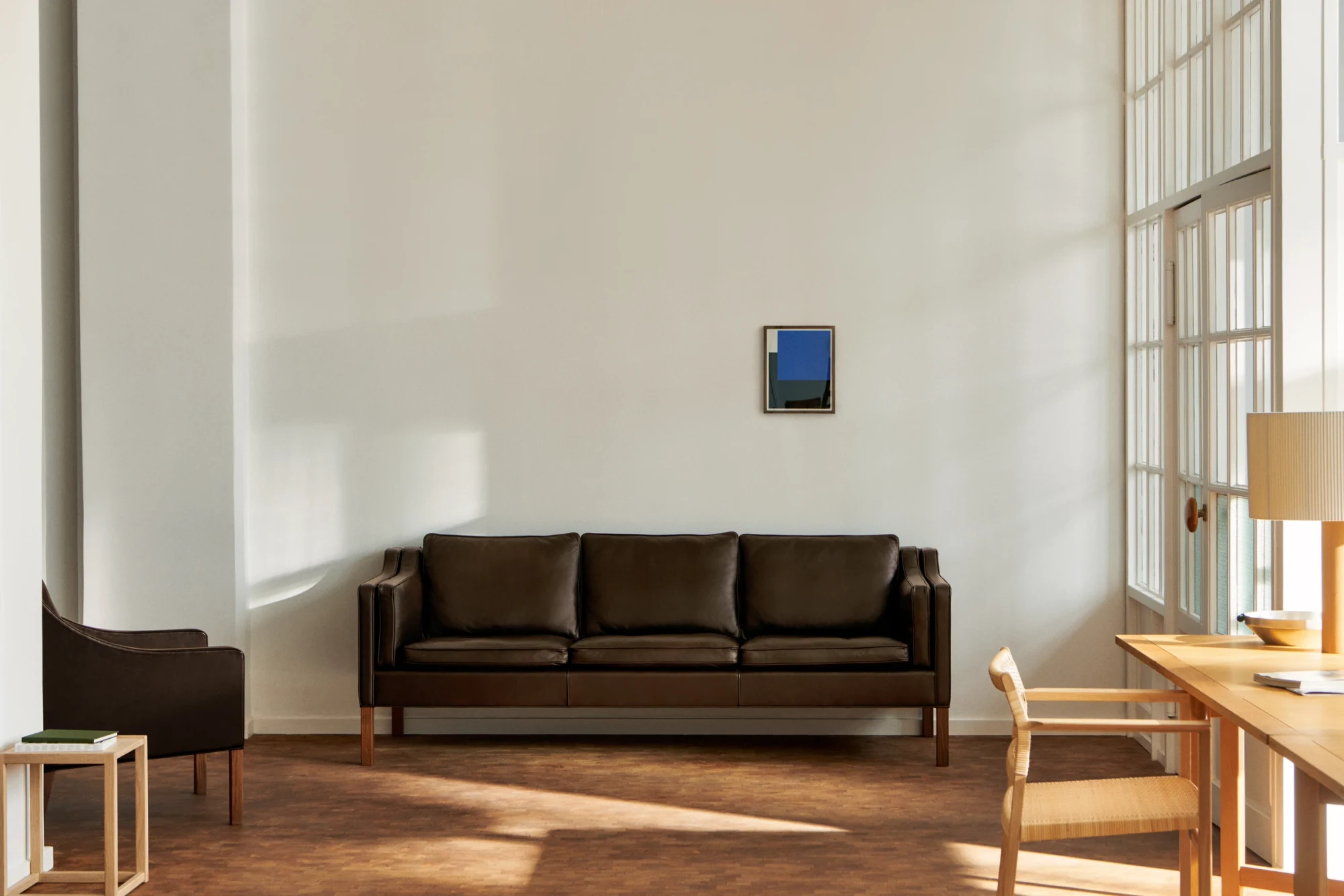 Le canapé le long d'un mur blanc dans une pièce haute aux grandes fenêtres, avec un bureau et des chaises sur les côtés
