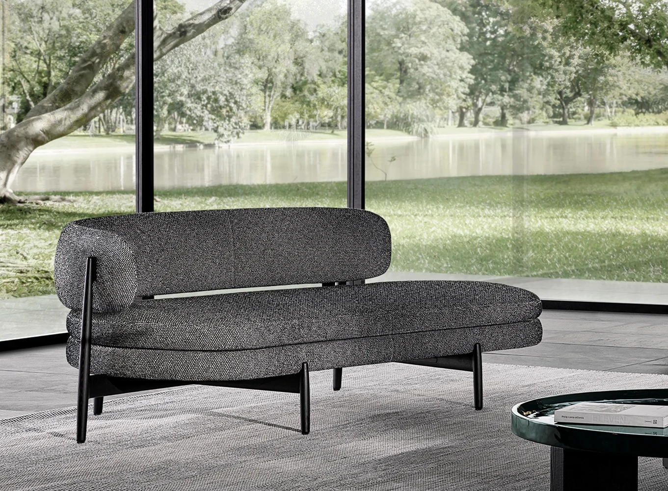 Dark upholstered sofa on slender legs with a round table in front of a lake view, official Minotti photo