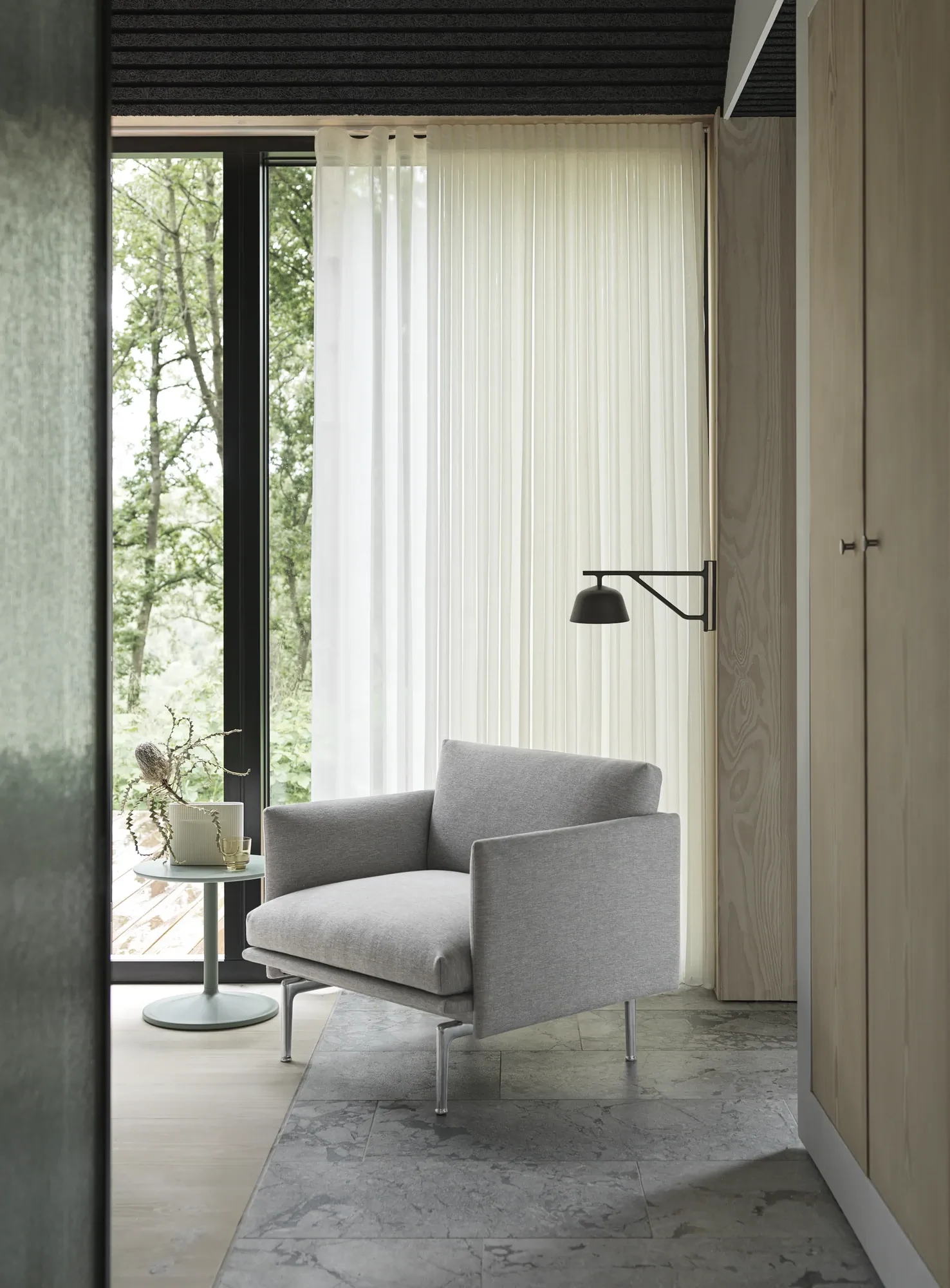 Outline Studio Chair vor einem hohen Fenster mit Vorhang, einer Wandleuchte und einem kleinen Beistelltisch