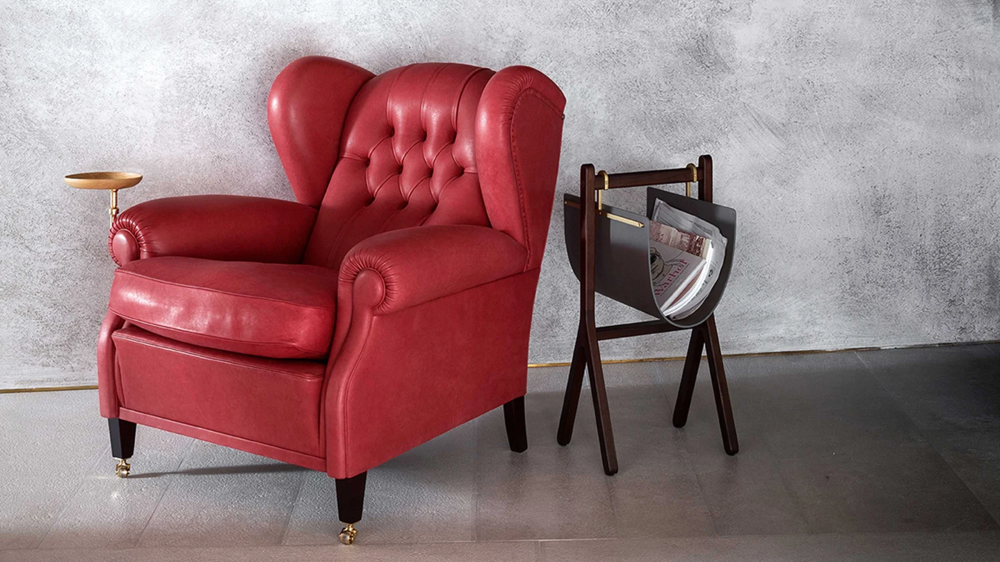 Fauteuil capitonné rouge à côté d'un support sombre sur un mur gris