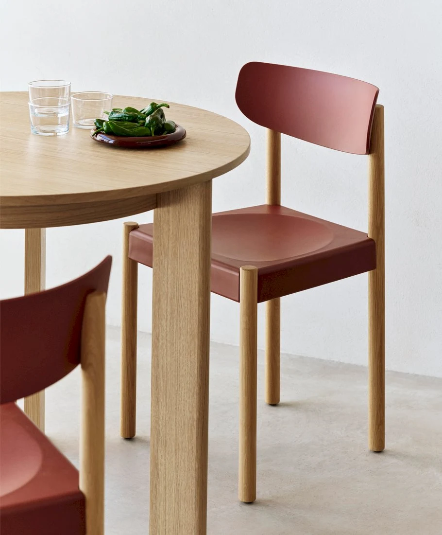 Two chairs with red shells and light wooden legs at a round wooden table with glasses and a plate