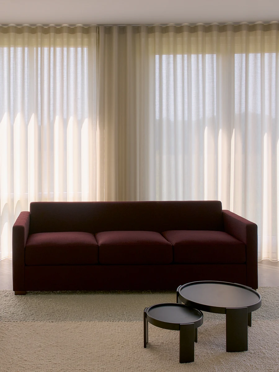 Three-seater sofa in dark red upholstery, with two low round tables in front