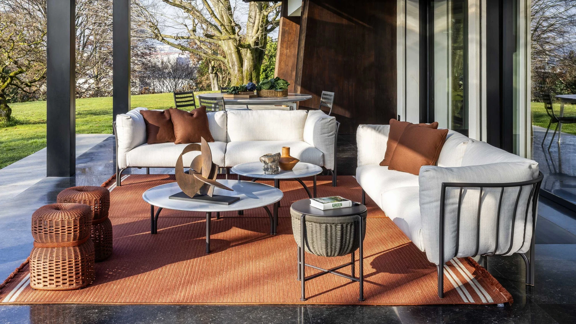 Two sofas with cushions and dark metal frames, round low tables and a red rug outdoors