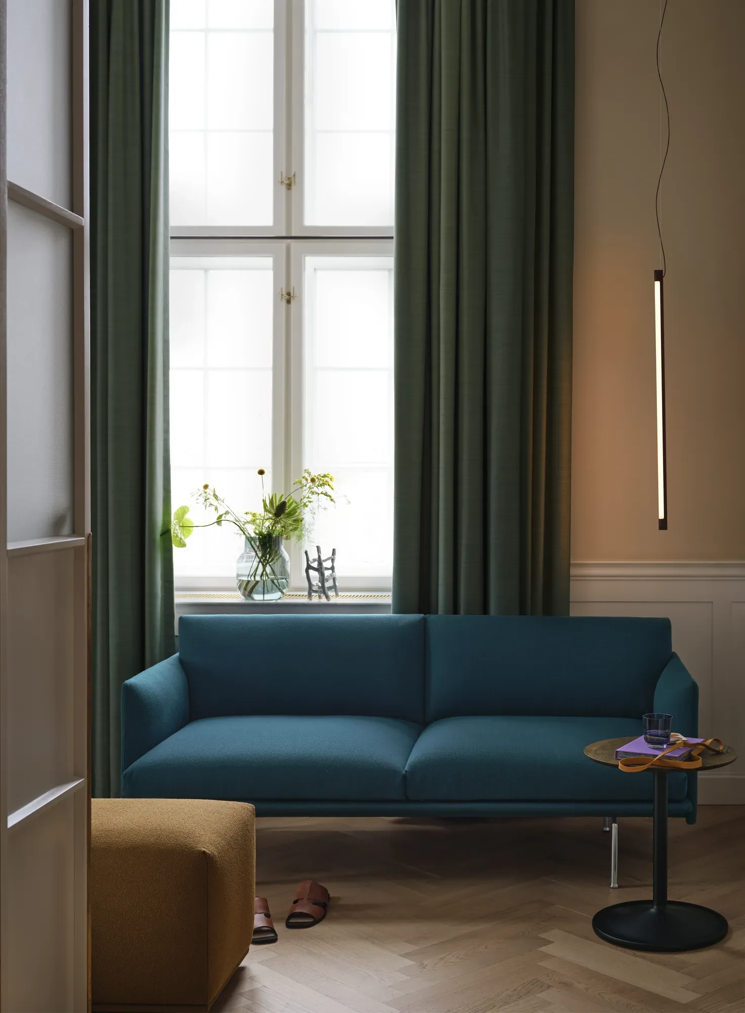 Outline Studio Sofa beside long curtains and a window, with a small round table at its side
