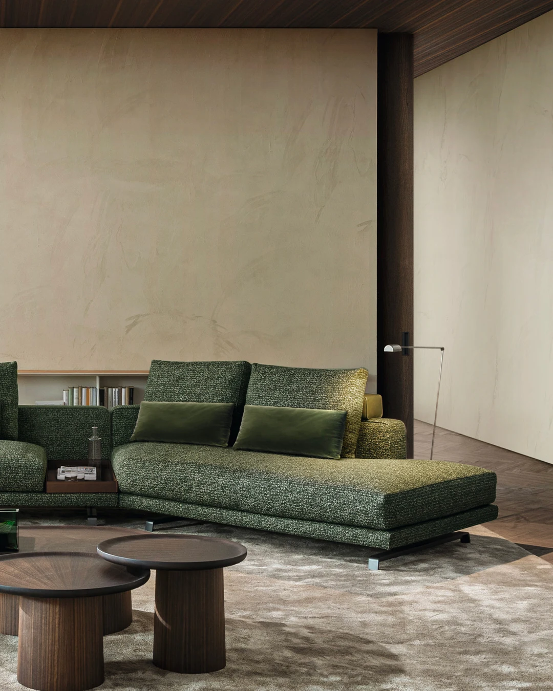 Green sofa composition with a chaise in a room with a plaster wall, shelves and round tables
