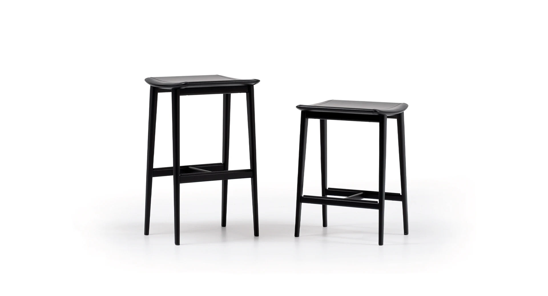 Two stools of different heights with a flat saddle-hide seat and a footrest