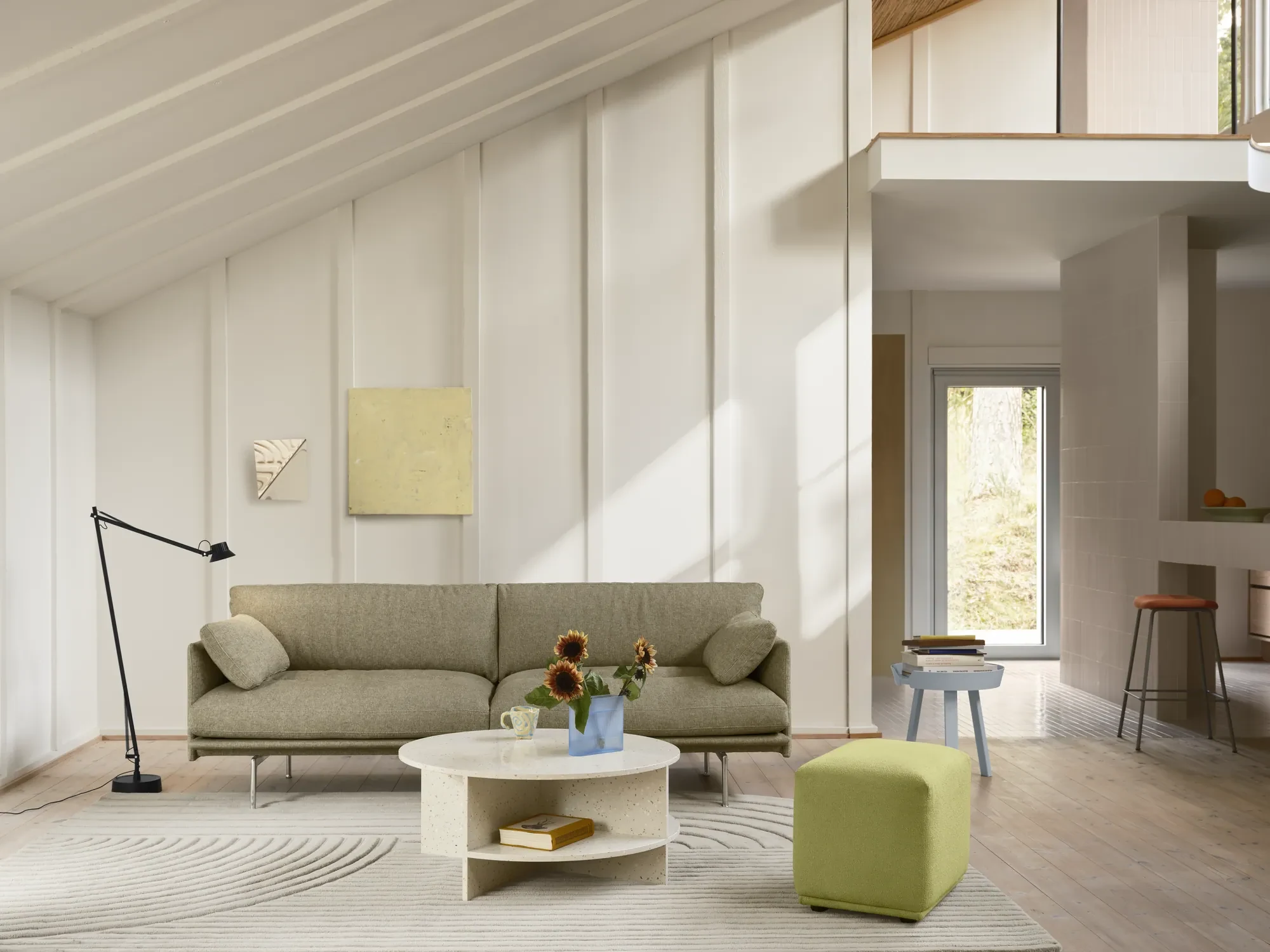 Sofa seen across a room, with a floor lamp, a round low table and a cube-shaped seat