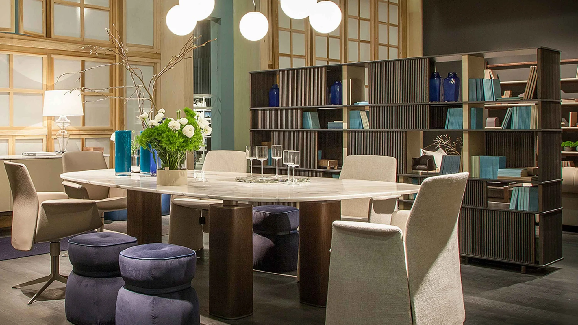 Table with chairs, stools and shelving around it in a room with spherical pendant lights