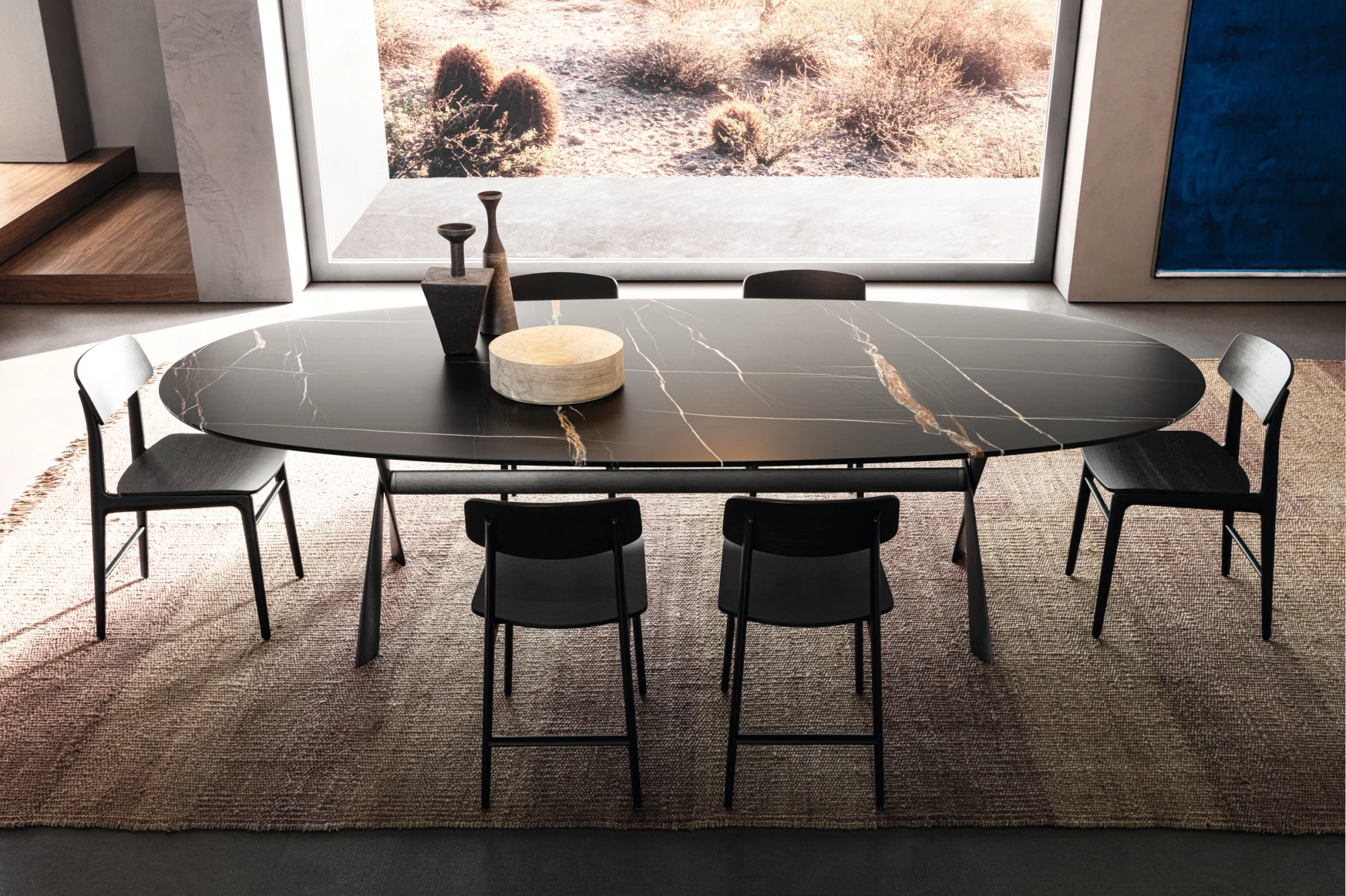 Long oval table with chairs around it, in a room with a large window onto a landscape