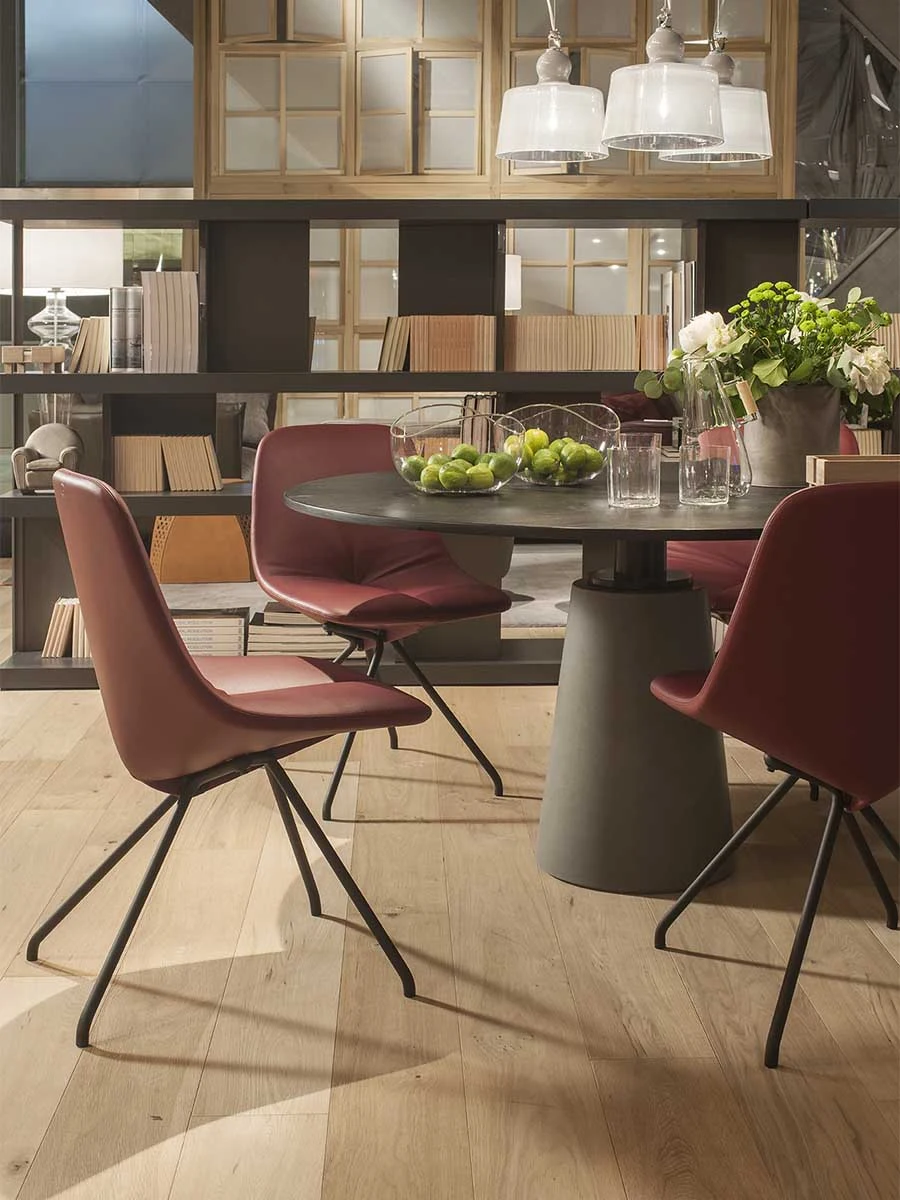 Round table with a bowl of fruit on it and red chairs around it in front of shelves