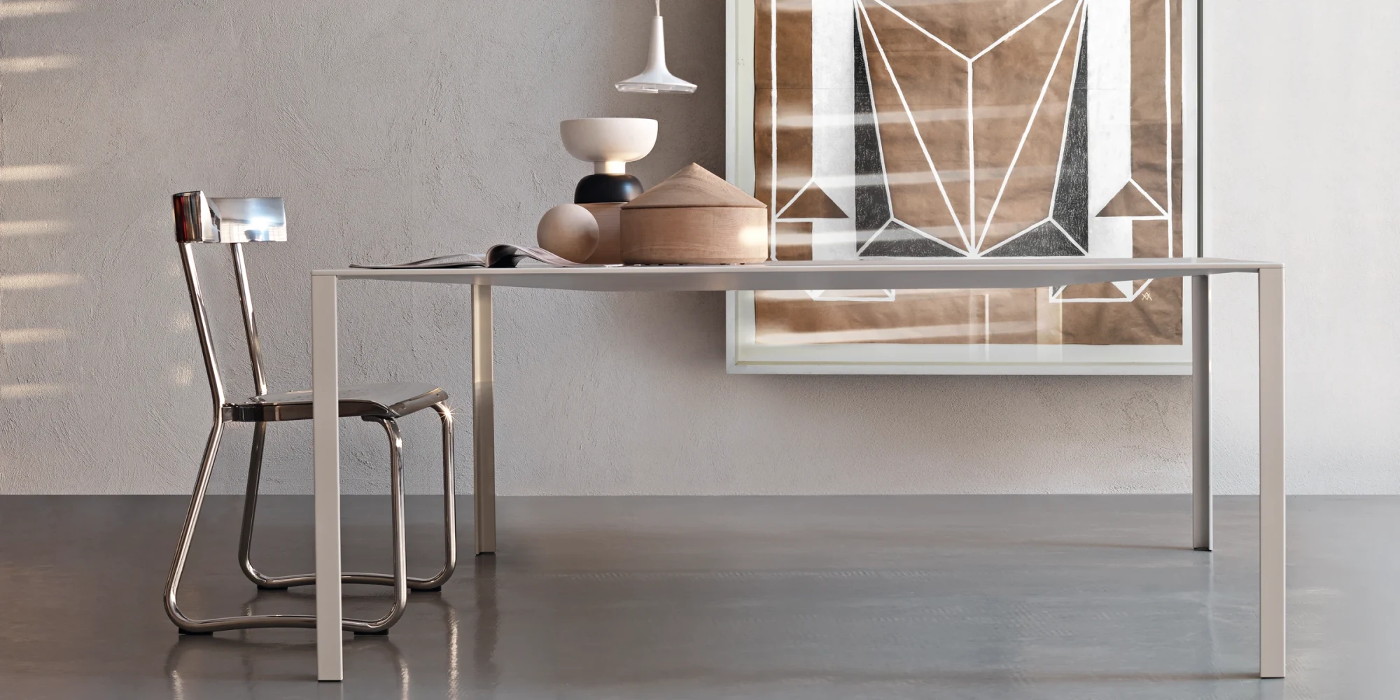 Long table with straight legs against a wall, with a chair at its left end and objects on it