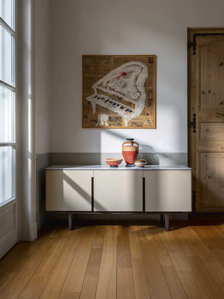 Cabinet with three doors in a room with tall windows and a framed picture on the wall