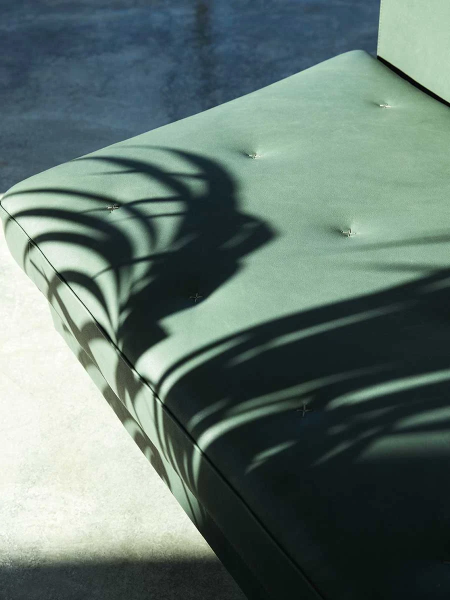 Close view of the tufted seat of a green sofa in strong light