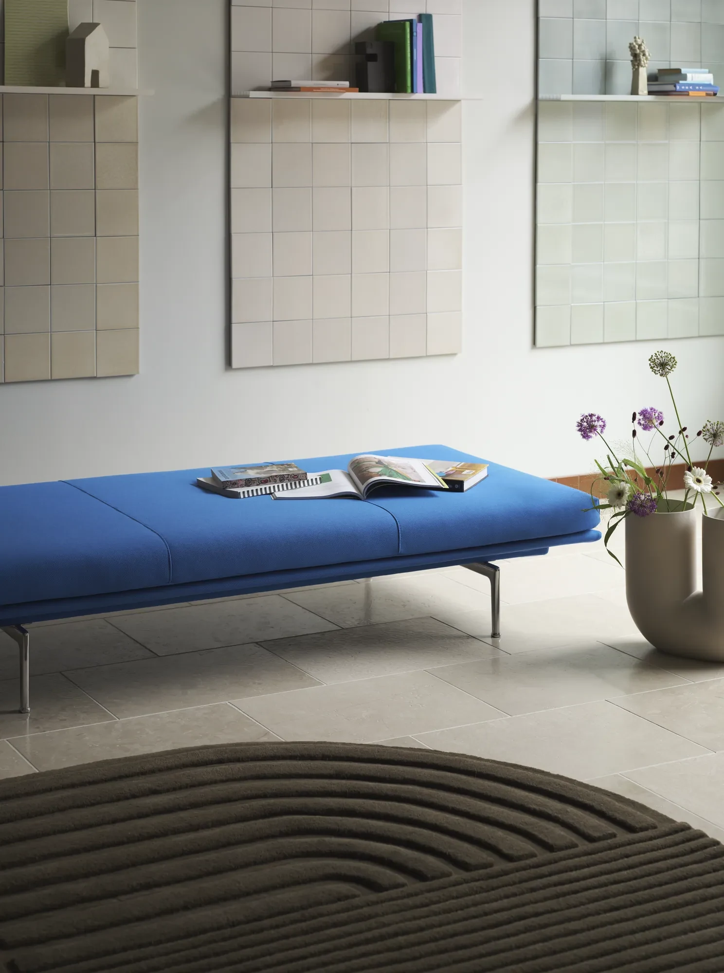 Outline Daybed with magazines on the seat, wall panels with shelves, a rug and a vase of flowers